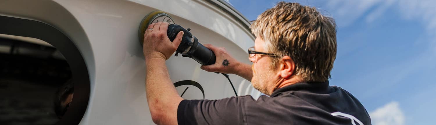 Mitarbeiter von MaRe Boote poliert den Rumpf eines Motorboots bei der Bootsaufbereitung