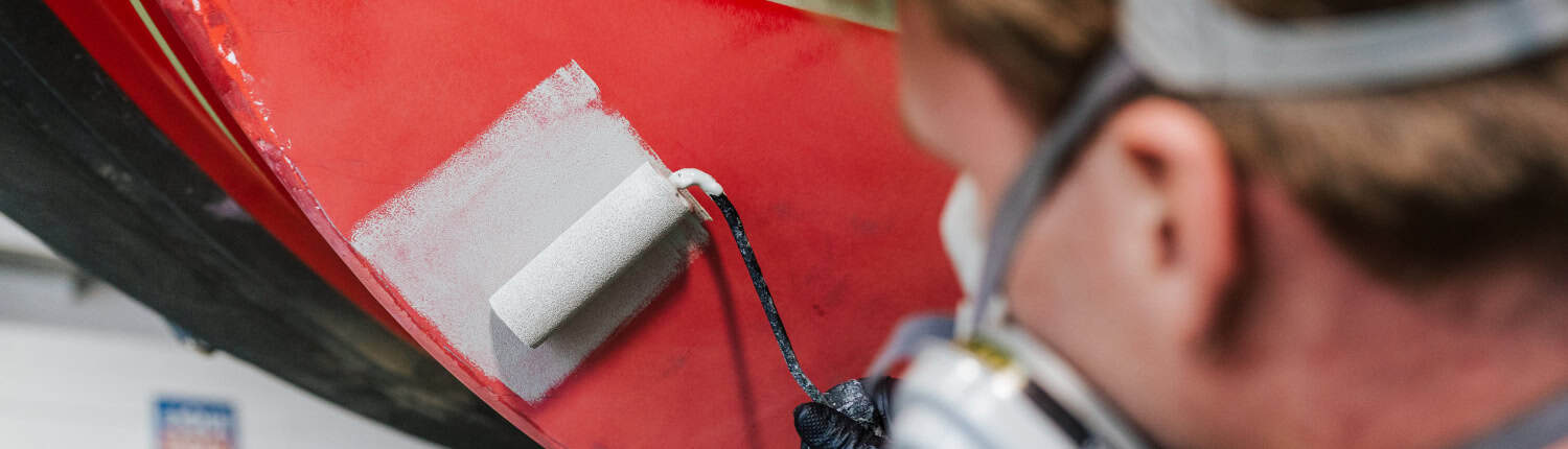 Mitarbeiter von MaRe Boote trägt rotes Antifouling mit der Rolle auf den Bootsrumpf auf